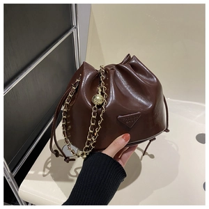 Detail view of brown glossy bucket bag featuring gold chain and fashion logo patch