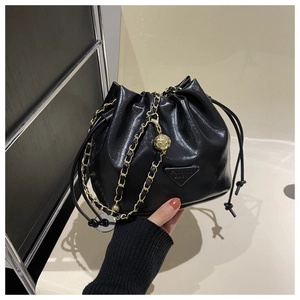 Detail of black drawstring bucket bag with gold chain and hollow metal ball charm