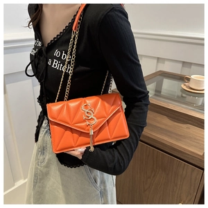 Detail of orange quilted crossbody bag with gold chain strap and stylish tassel fringe
