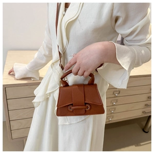 Close-up of mini brown leather handbag with signature circular handle on white shirt