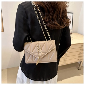 Detail der apricotfarbenen Stepptasche mit goldenem S-Logo und Metallquaste