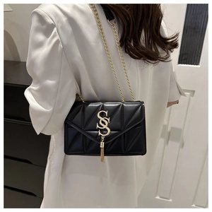 Detail shot of a black quilted crossbody bag with gold chain strap and tassel charm