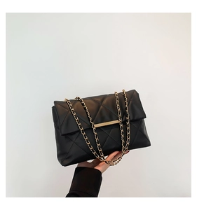 Detail of black quilted shoulder bag with gold chain strap and metallic bar closure