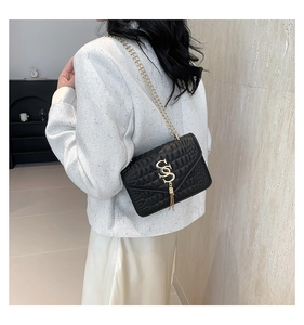 Détail d'un sac bandoulière matelassé noir avec chaîne dorée porté par un mannequin