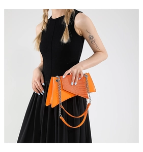 Detail of bright orange asymmetric handbag with crocodile texture and silver chain strap