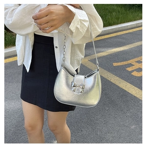 Silver crescent shoulder bag with metallic bow buckle and chain strap on a model