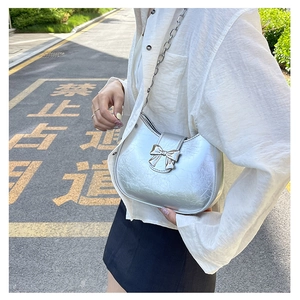 Detail of silver metallic shoulder bag featuring bow decoration and chain strap