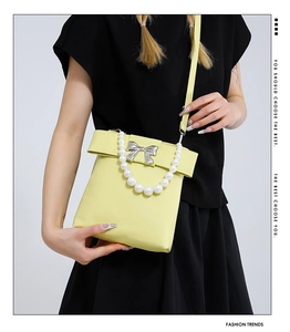 Detail of yellow bow shoulder bag featuring pearl handle and silver metal accents