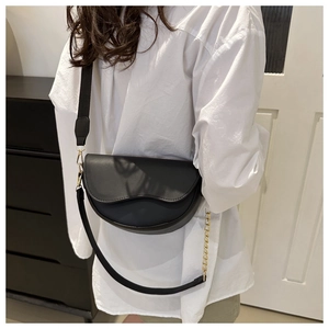 Détail du sac selle noir avec large bandoulière en tissu et chaîne décorative dorée