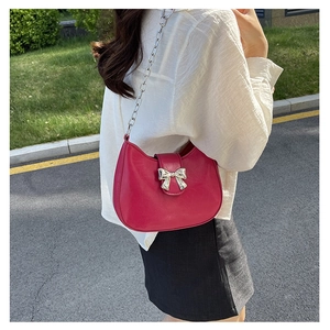 Detailed view of magenta semi-circular bag with silver bow accent and chain strap