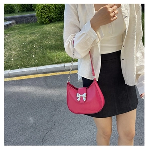 Detail of hot pink half-moon shoulder bag with silver bow accent and chain strap