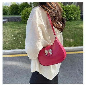 Close-up of pink underarm bag with silver bow detail in a natural street setting