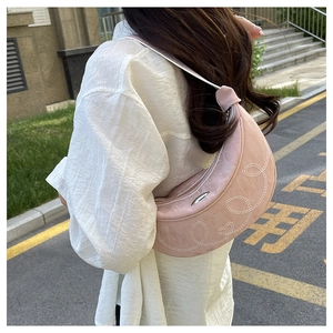Close-up of pink crescent saddle bag with white floral embroidery and heart stitching