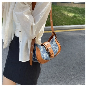 Detail of denim and leather patchwork saddle bag with silver buckle and adjustable strap