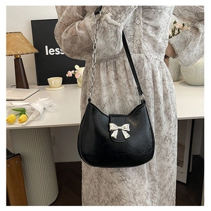 Detail of black semi-circular shoulder bag with silver bow accent and metal chain strap