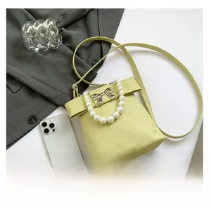 Detail of light green pearl chain bag featuring a decorative metal bow and smooth leather