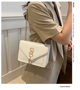 Close-up of beige chain shoulder bag featuring gold logo and stylish tassel detail