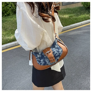 Detail view of denim tie-dye saddle bag with brown leather trim and metal buckle
