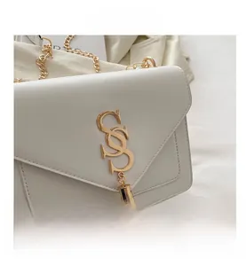 Close-up of white envelope crossbody bag featuring a gold SS logo and elegant metal tassel