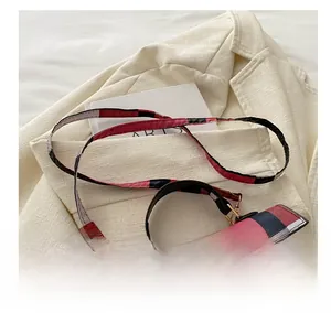 Detail of red and black plaid crossbody bag with gold metal buckle and adjustable strap
