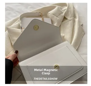 Detail view of the golden magnetic snap closure on a white patent leather flap bag