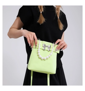 Détail du sac bandoulière vert néon avec poignée en perles et nœud argenté sur noir