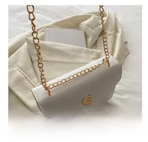 Detail of a cream envelope bag with gold chain strap next to a white blazer