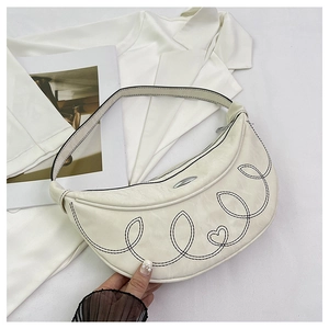 Detail of creamy white crescent bag featuring black embroidery and heart pattern