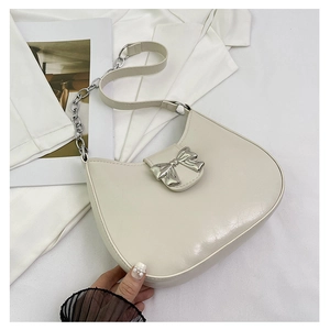 Close-up of semi-circle crossbody bag with silver bow buckle and cream faux leather finish