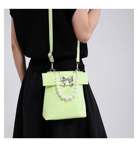 Detail of neon green PU leather bag with silver bow and decorative pearl handle strap