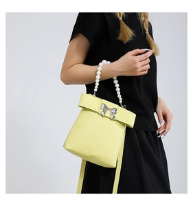 Detail of yellow crossbody bag featuring a pearl handle and silver bow decoration