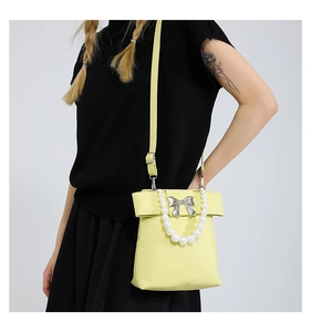 Detail view of yellow crossbody bag with white pearl handle and silver bow hardware