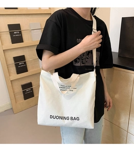 Detail of off-white canvas tote bag featuring stylish text and wide shoulder strap