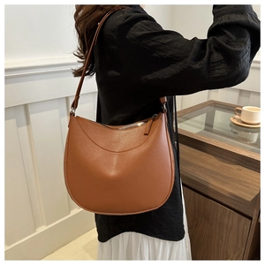 Brown half-moon saddle bag in lychee pattern leather worn by model in minimalist setting