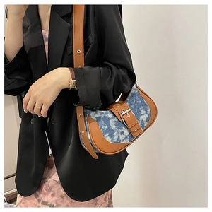 Close-up of retro denim patchwork crescent bag with brown leather trim and metal buckles