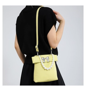 Détail du sac bandoulière jaune avec poignée en perles et nœud argenté sur noir