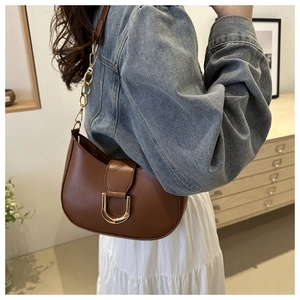 Brown leather crescent bag with gold horseshoe buckle and chain detail on model