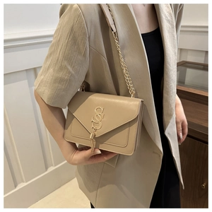 Khaki crossbody bag with gold hardware and leather tassels worn by a model in a beige suit