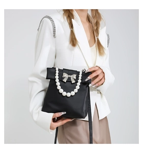 Detail of black bow handbag with pearl handle and silver ornament on white blazer