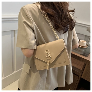 Detail of khaki flap bag with gold chain strap, metal logo and tassel on model