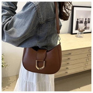 Detail of a brown leather crescent shoulder bag with elegant golden horseshoe buckle