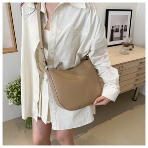 Detail view of the khaki pebbled leather crescent crossbody bag worn by a model