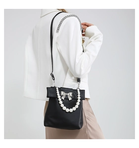 Detail of black leather bucket bag with silver bow buckle and white pearl handle strap