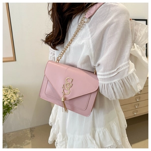 Detail of light pink envelope bag with gold SSS logo and metal tassel on a model
