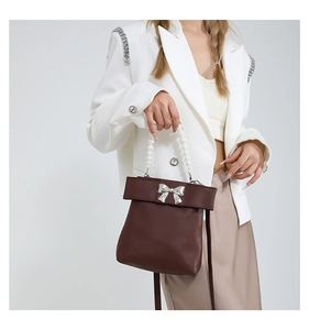 Detail of dark brown faux leather bag with silver metal bow and pearl handle