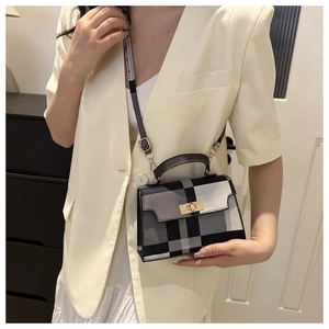 Classic black and white plaid crossbody square bag with gold buckle on a beige blazer