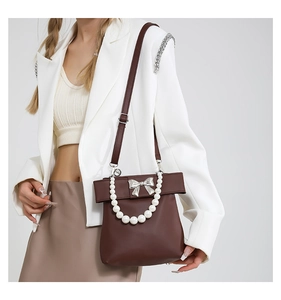 Close-up of brown leather handbag with silver bow hardware and pearl handle detail