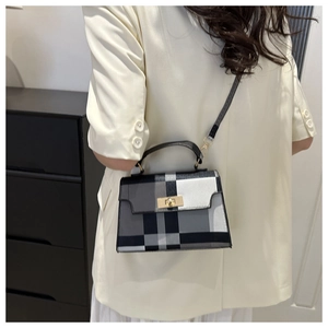 Detail of colorful plaid crossbody bag with gold buckle on a model in indoor setting