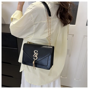 Detail of black leather envelope bag showing golden logo tassel and metal chain strap