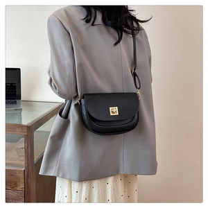 Sacoche noire avec boucle dorée portée par un mannequin dans un bureau de style moderne